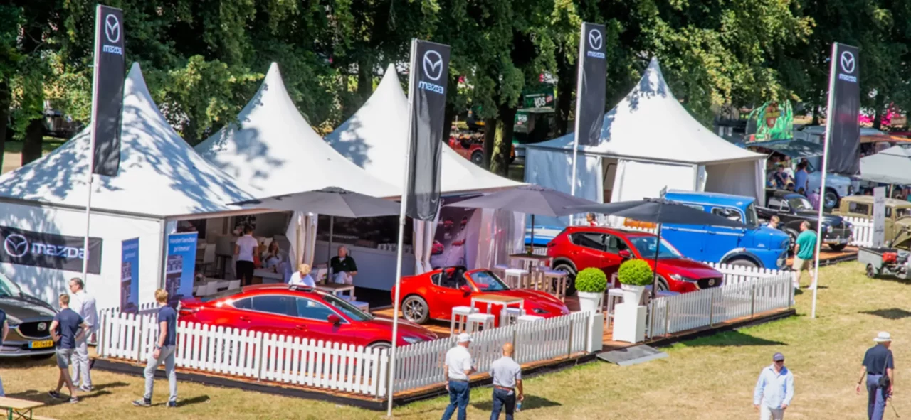 Gereihte, verbundene VIP-Pagoden von Zeltverleih Intersettle mit Terrasse und Flaggen zur Präsentation von Autos