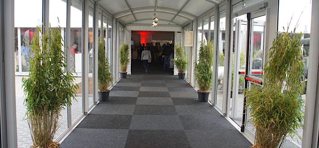 Blick in die Eventlocation durch den Eingang der Pergola Walkway mit Teppichboden, Eventstyling und Mietpflanzen von Intersettle Zeltvermietung